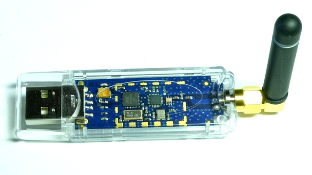 USB enabled CC1101 controller board with RP-SMA socket and l/4 antenna in transparent plastic case. Optional HF-shield not mounted.