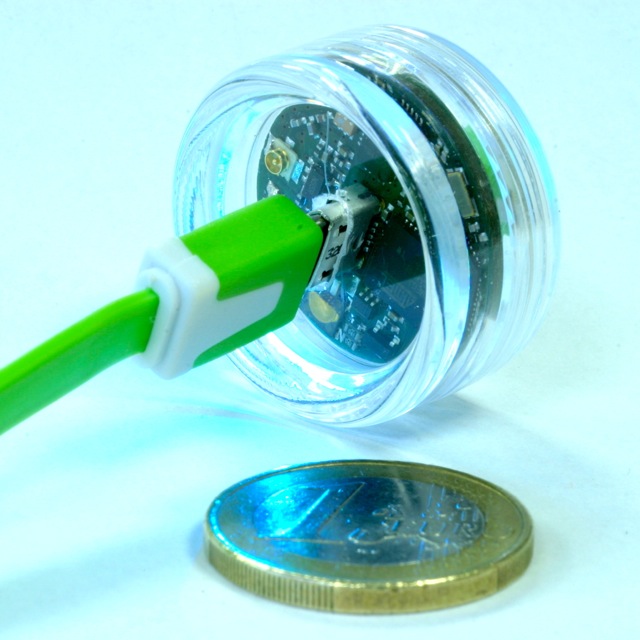 Round board in a transparent case next to a one-euro coin for scale